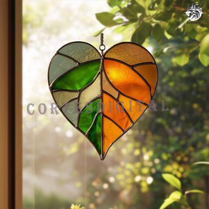 May include: Stained glass heart-shaped suncatcher with a leaf design. The heart is divided into sections of green, yellow, and orange glass, with a metal frame and a loop for hanging. The word "COR" is partially visible.