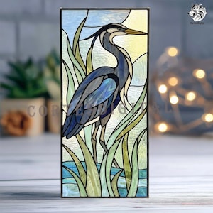 May include: Stained glass panel featuring a blue heron standing in water among reeds. The artwork has a rectangular shape with a black frame. The heron is depicted in shades of blue, gray, and white, with a yellow beak. The background includes a blue sky and yellow highlights.