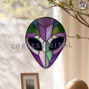 May include: Stained glass alien head in shades of purple, green, and blue. The artwork features a geometric design with a black outline and the text "CORES DIGITAL". The alien head is hanging in front of a window.