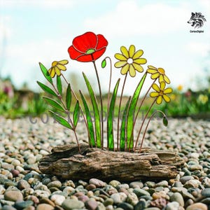 Peut inclure: Composition florale en vitrail avec un coquelicot rouge et des marguerites jaunes, des feuilles et des tiges vertes. Les fleurs sont posées sur du bois flotté et reposent sur un lit de galets.