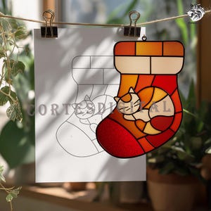 Peut inclure: Ornement de Noël en vitrail représentant une chaussette de Noël avec un chat endormi. L'ornement présente des nuances de rouge, d'orange et de jaune. Un dessin au trait de la chaussette et du chat est visible en arrière-plan. Le texte "Cortes Digital" est visible.