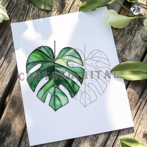 May include: A stained glass Monstera leaf design in shades of green, with a detailed outline and numbered sections. The image is on a white paper, with the text "CONFIDENTIAL DIGITAL" partially visible. The background is a wooden surface.