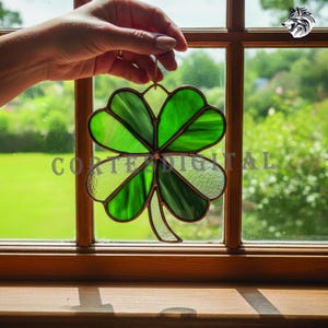May include: A stained glass four-leaf clover suncatcher with shades of green and a copper-colored frame. The clover is suspended by a thin gold-colored wire. The text "CORTE DIGITAL" is visible on the bottom left.