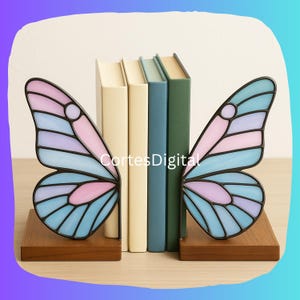 May include: Butterfly wing bookends in shades of blue, pink, and purple, with a black outline, sit on a wooden base. The bookends flank a row of books with cream, blue, and green spines. The text "Cortes Digital" is visible.