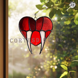 May include: A stained glass heart suncatcher with a vampire fangs design. The heart is red with white fangs and black outlines. The text "CORTES DIGITAL" is visible on the bottom of the heart.