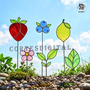 Puede incluir: Una colección de coloridas estacas de jardín de vidrieras con forma de fresa, arándanos, limón, flor y hojas. Las estacas están colocadas en un parterre con el texto "Cortes Digital".