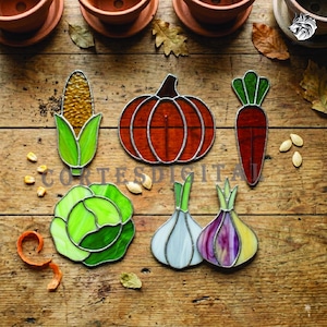 May include: Stained glass vegetable ornaments including a corn cob, pumpkin, carrot, cabbage, and two onions. The ornaments are in shades of green, orange, red, and yellow. The text "CORTES DIGITAL" is visible on the image.