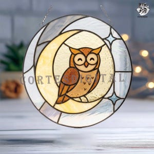 May include: A circular stained glass suncatcher featuring a brown owl perched on a yellow crescent moon. The background consists of translucent white glass panels with blue star accents. The text CORTESDIGITAL is printed across the center.