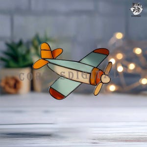 Pode incluir: Um avião de vitral em tons de laranja, azul claro e creme, delineado em preto. O avião tem uma hélice. O texto "Cortes Digital" é visível na imagem.