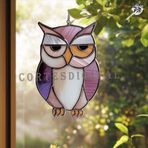 May include: Stained glass owl suncatcher with a silver metal frame. The owl features a color palette of purple, pink, white, and orange. The text "CORTES DIGITAL" is visible on the owl. The suncatcher is hanging in front of a window.