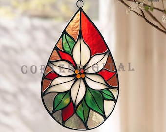 May include: Stained glass teardrop ornament featuring a poinsettia design. The ornament has a black metal frame and a variety of colors, including red, green, white, and brown. The ornament is hanging from a black hook.