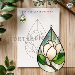 May include: A stained glass pattern featuring a white magnolia flower with green leaves and a brown stem, set against a light green background. The design is in a teardrop shape with a black metal frame. The text "STAINED GLASS PATTERN" is at the top.