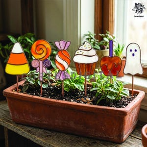 May include: A set of six stained glass garden stakes featuring a candy corn, a swirl lollipop, a wrapped candy, a cupcake, a caramel apple, and a ghost. Each piece is crafted with colourful glass and metal borders, designed to be inserted into soil.