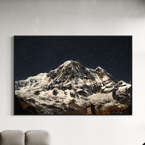 Puede incluir: Un pico de montaña nevado se eleva contra un cielo nocturno oscuro lleno de estrellas. La montaña está iluminada por la luz de la luna, creando un contraste dramático entre la nieve blanca y el cielo negro.