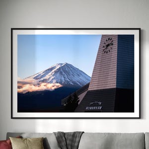 May include: A black framed photograph of Mount Fuji with a clock tower in the foreground. The clock tower has a white and gray exterior with a black roof. The text "グリーンシーズン" and "河口湖温泉郷" is visible on the tower.