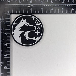 May include: A black and white round emblem featuring a wolf's head profile and the letters "AWA" with a plus sign. The emblem is approximately 3 inches in diameter.