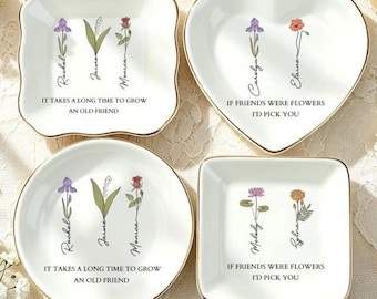 May include: Four white ceramic trinket dishes with gold-toned rims, featuring floral illustrations and text. Two dishes display the text 'IT TAKES A LONG TIME TO GROW AN OLD FRIEND' and two display 'IF FRIENDS WERE FLOWERS I'D PICK YOU' with names.