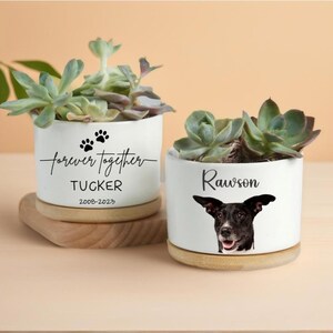 May include: Two white ceramic plant pots with succulents, each on a wooden coaster. One pot has the text "forever together" with paw prints, the name "Tucker", and dates. The other has a dog portrait and the name "Rawson".
