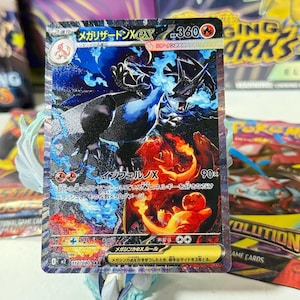 May include: A Mega Charizard X EX trading card featuring a dark blue dragon with blue flames, a red Charizard, and a small Charmander. The card displays 360 HP, the text Mega Charizard X, and Japanese characters throughout the card design.