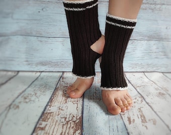 May include: Dark brown leg warmers with white trim and a white stripe near the top. The leg warmers have a heel cutout. The background is a light blue and white wooden surface. The leg warmers are shown on a person's legs.