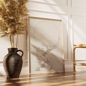 Puede incluir: Una impresi&oacute;n enmarcada de un dibujo cl&aacute;sico que representa a Atlas sosteniendo una esfera. La obra de arte est&aacute; en un marco dorado y se apoya contra una pared blanca. Un jarr&oacute;n marr&oacute;n oscuro con plantas secas y una mesa auxiliar de bamb&uacute; tambi&eacute;n est&aacute;n en la imagen.