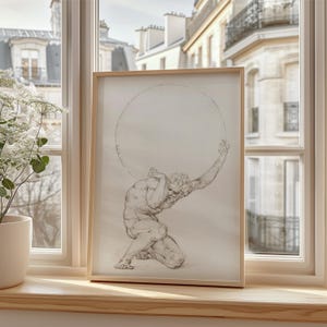 Puede incluir: Una impresi&oacute;n enmarcada de un dibujo cl&aacute;sico que representa a Atlas, una figura mitol&oacute;gica, sosteniendo una gran esfera. La obra de arte est&aacute; en un marco de madera clara, frente a una ventana con vistas a edificios. El dibujo es en tonos grises y beige.