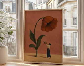 May include: A framed art print featuring a large, deep red poppy flower with green leaves on a muted terracotta background. A small figure stands at the base of the flower, holding a watering can to tend to the plant on a sandy-colored surface.
