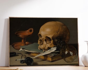 May include: A framed still life painting featuring a human skull, a glass, a book, a feather, and an oil lamp. The artwork has a dark background and is displayed on a wooden shelf.