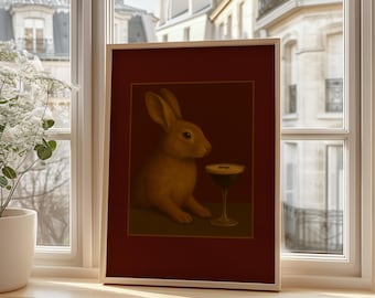 May include: A framed art print featuring a rabbit and a cocktail. The rabbit is depicted in shades of tan and brown, with a dark cocktail in a stemmed glass. The artwork is set against a dark red background, framed in a light wood.