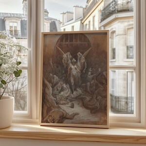 May include: A framed artwork featuring a dramatic scene with figures in shades of brown and gray. The central figure, with outstretched arms, is illuminated by light. The artwork is displayed on a wooden windowsill, with a view of a European cityscape.