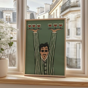 May include: A framed art print featuring a stylized illustration of a man in a striped suit holding trays of wine glasses. The artwork has a green background and is set in a wooden frame, placed on a windowsill.