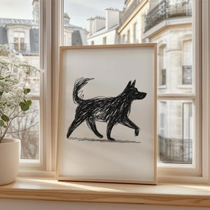 May include: A framed art print featuring a black dog illustration. The dog is depicted in a walking pose with a scribbled, textured style. The artwork is displayed on a windowsill with a view of a city.