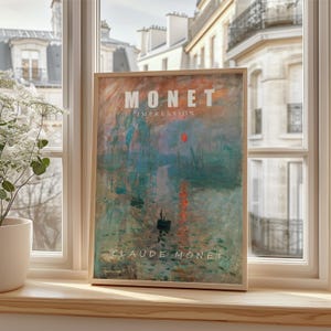 May include: A framed print of Claude Monet's Impression, Sunrise painting. The artwork features a harbor scene with boats, a red sun, and the text "MONET IMPRESSION" at the top and "CLAUDE MONET" at the bottom. The frame is light brown.
