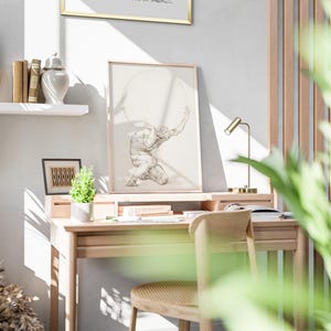 Puede incluir: Un escritorio de madera clara con una impresi&oacute;n enmarcada de un hombre sosteniendo una esfera. Una peque&ntilde;a l&aacute;mpara de escritorio dorada y una silla de madera est&aacute;n frente al escritorio. Una peque&ntilde;a planta y libros est&aacute;n en el escritorio.