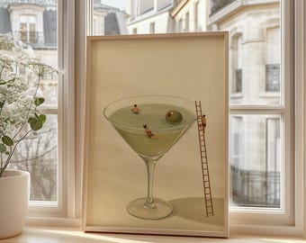 May include: A framed art print featuring a large martini glass filled with pale green liquid. Two small figures are swimming in the liquid, while a third figure climbs a tall wooden ladder leaning against the rim of the glass. A single green olive floats in the drink.