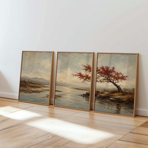 May include: Three framed landscape paintings displayed side by side, featuring a river scene with a prominent tree displaying vibrant red autumn leaves, rolling hills in the distance, and a soft, cloudy sky rendered in muted earth tones.