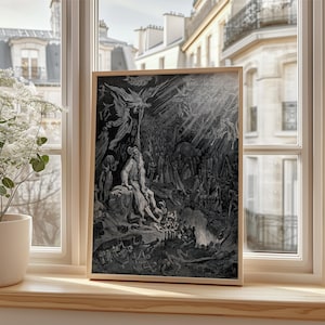 May include: A framed black and white illustration depicting a dramatic scene with figures, angels, and a crowd. The artwork is in a light wood frame, set on a wooden windowsill, with a view of buildings and a plant in a white pot.