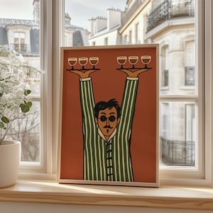 Op de afbeelding: Een ingelijste kunstdruk met een gestileerde illustratie van een persoon met donker haar, een snor en een ronde bril, gekleed in een groen-wit gestreept overhemd. De persoon houdt twee dienbladen boven het hoofd, elk met drie glazen erop.