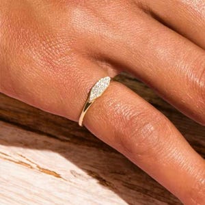 Peut inclure: Une bague en or avec une petite pierre en forme de diamant sertie au centre. La pierre est entourée de diamants plus petits.