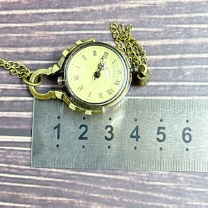 May include: Vintage brass pocket watch with a cream face and Roman numerals. The watch has a decorative frame and chain. The watch face is approximately 3.8 cm in diameter.