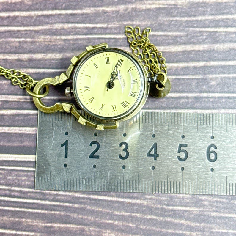 May include: Vintage brass pocket watch with a cream face and Roman numerals. The watch has a decorative frame and chain. The watch face is approximately 3.8 cm in diameter.