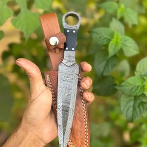 Op de afbeelding: Een zilveren dolk met een zwarte handgreep en een leren schede. De dolk heeft een uniek, gepatenteerd lemmet.