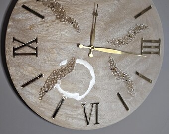 May include: A round, white clock with gold Roman numeral markings and gold hands. The clock face is decorated with small, white beads.