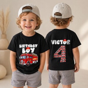 May include: A black short-sleeved t-shirt featuring a red fire truck graphic with the text Birthday Boy on the front and the name Victor with the number 4 composed of small fire truck graphics on the back, paired with gray shorts and a cap.