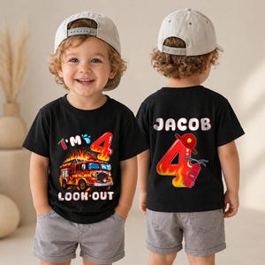 May include: Two black t-shirts featuring a fire truck graphic. The front shirt displays a fire truck with flames, the text I'M 4 LOOK OUT, and a fire extinguisher. The back shirt shows the name JACOB, the number 4 with flames, and a fire helmet.