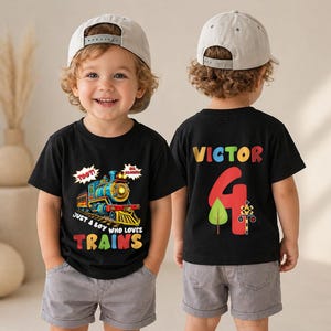 May include: A black t-shirt featuring a colorful steam train graphic with the text TOOT! ALL ABOARD! JUST A BOY WHO LOVES TRAINS on the front, and the name VICTOR with the number 4, a tree, and a railroad crossing sign on the back.