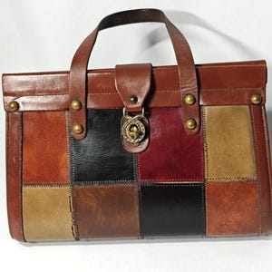 May include: A rectangular handbag featuring a patchwork design of leather squares in shades of brown, black, tan, and deep red. The bag includes a brown leather handle, a top flap with a gold-toned metal twist lock closure, and brass studs.