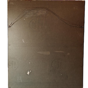 May include: The back of a framed picture with a brown wooden frame. The back of the frame is made of a light brown cardboard material. There are three circular stamps on the back of the frame. The stamps are all in black and white and have text that is difficult to read.