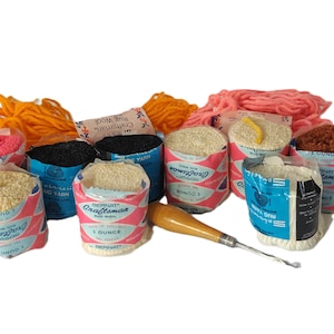 May include: A collection of colorful rug-making supplies. The image features various bundles of yarn in shades of pink, orange, black, and cream, along with a wooden-handled rug hook. The yarn is packaged in vintage-style paper containers.