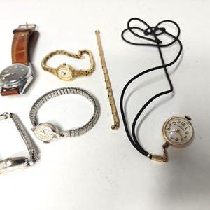 May include: A collection of timepieces including a watch with a brown leather strap, a gold-tone watch with a link bracelet, a silver-tone watch with an expansion band, a separate silver-tone watch band, a gold-tone chain, and a pendant watch on a cord.